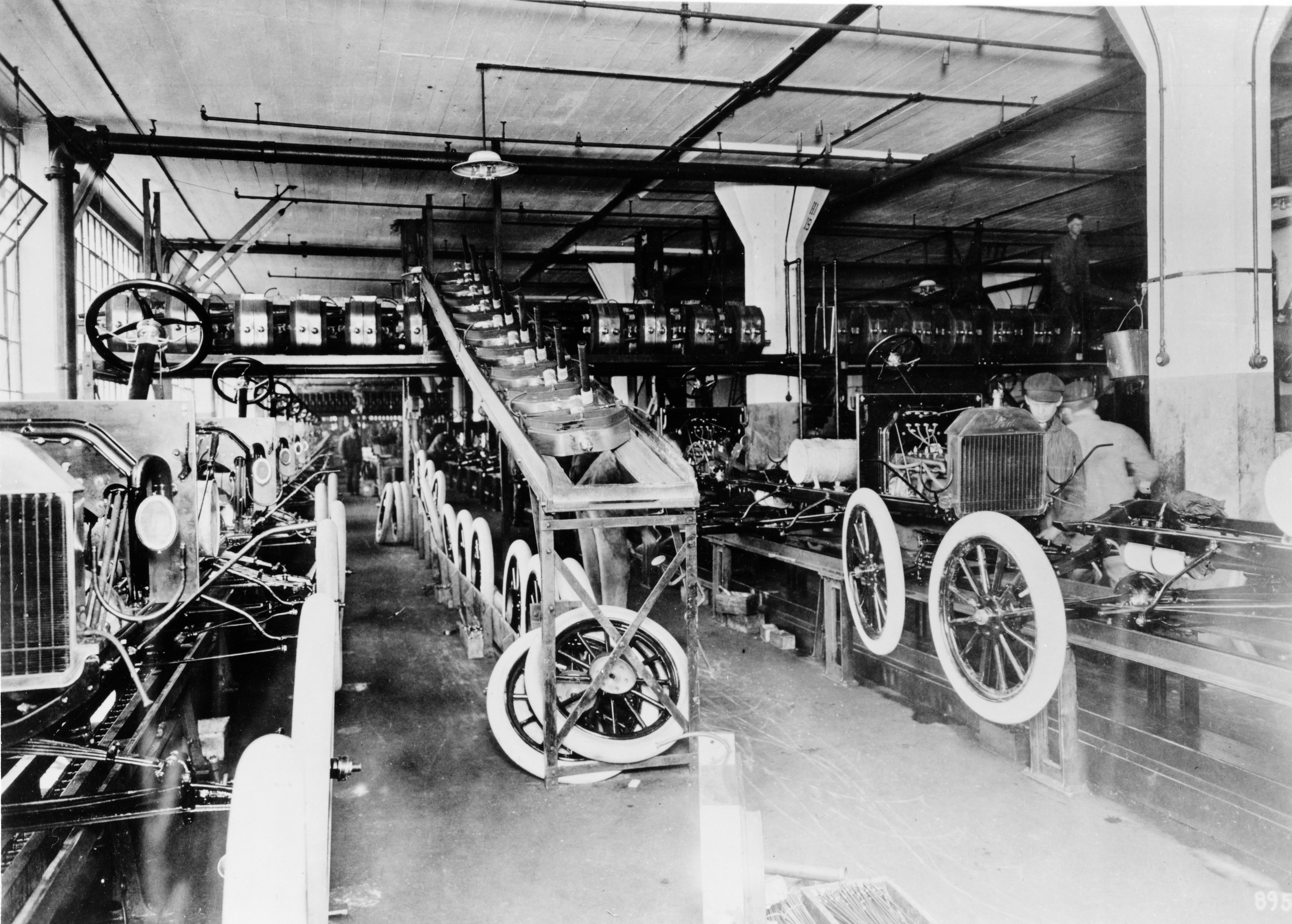 An old-school assembly line with many tires and several male workers in old-fashioned clothes pictured in black and white.
